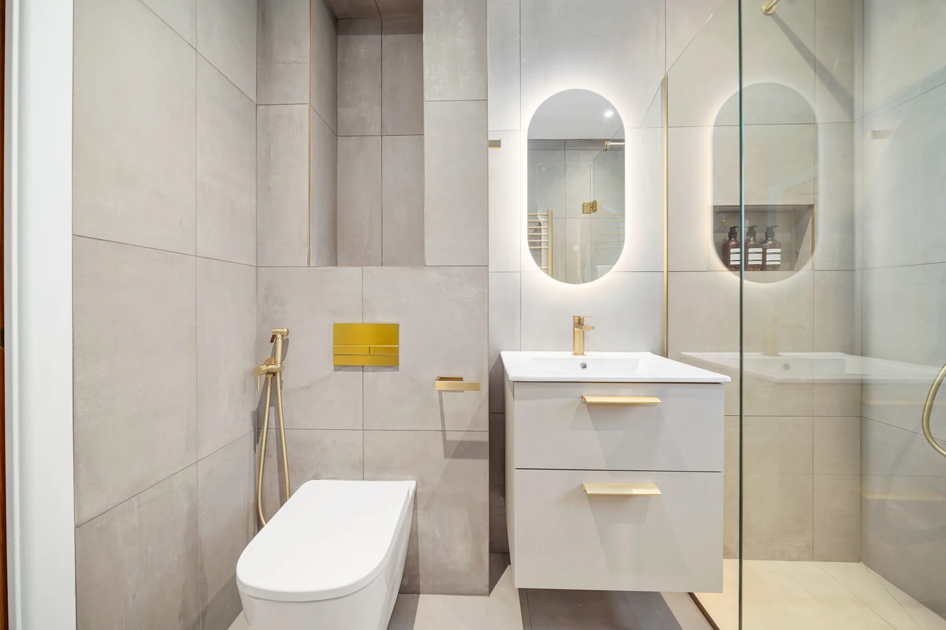 Completed compact bathroom with a framed shower screen, mirrored storage, a floating vanity and warm-metal details.