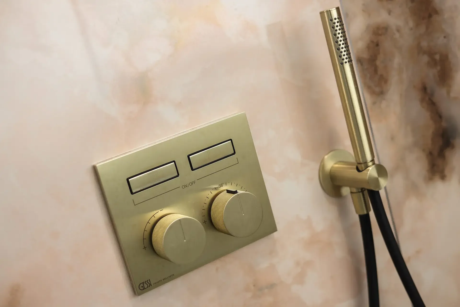 Warm-metal shower controls against a softly veined blush stone surface.