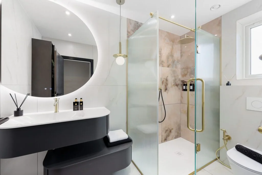 Luxury bathroom in Ilford with a black floating vanity, curved backlit mirror and fluted-glass walk-in shower.