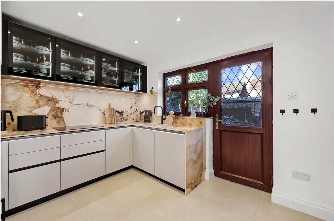 Contemporary Chigwell kitchen with white handleless furniture, dark glazed wall cabinets and strongly veined stone surfaces.
